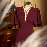 Mannequin wearing a burgundy dress with gold necklace against a wooden cabinet background