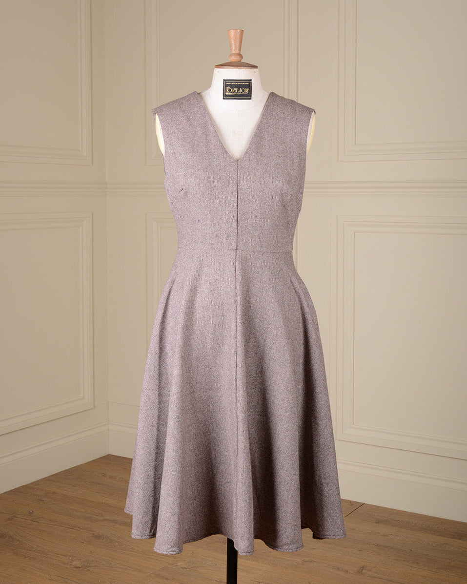 A sleeveless V-neck A-line dress in a textured taupe-gray fabric, displayed on a mannequin in a room with cream paneled walls and a wooden floor.