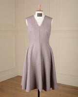 A sleeveless V-neck A-line dress in a textured taupe-gray fabric, displayed on a mannequin in a room with cream paneled walls and a wooden floor.