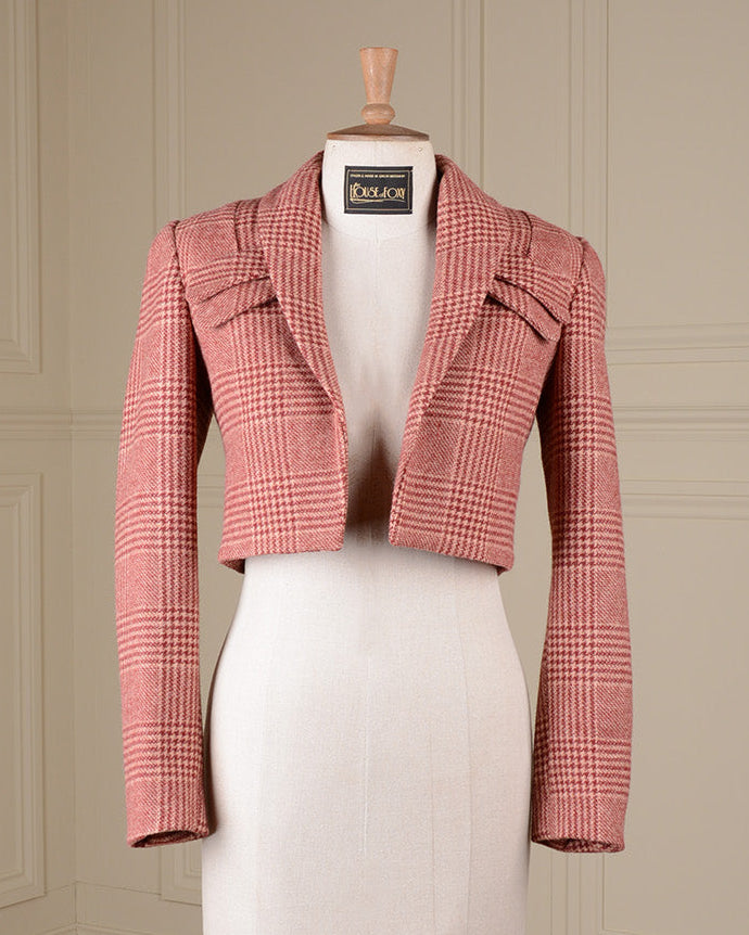 A pink and white houndstooth cropped jacket displayed on a white dress form mannequin, set against a cream paneled wall and wooden floor.