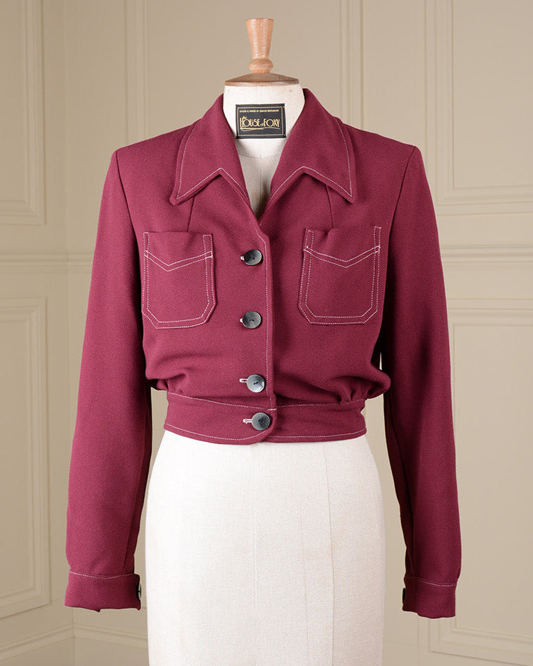 A cropped magenta pink utility jacket with contrast white stitching and dark buttons, displayed on a cream-colored dress form mannequin in front of a beige paneled wall.
