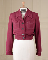 A cropped magenta pink utility jacket with contrast white stitching and dark buttons, displayed on a cream-colored dress form mannequin in front of a beige paneled wall.