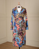 A long-sleeve wrap dress with a vibrant multicolor floral and abstract botanical print, displayed on a mannequin in front of a cream-colored paneled wall.