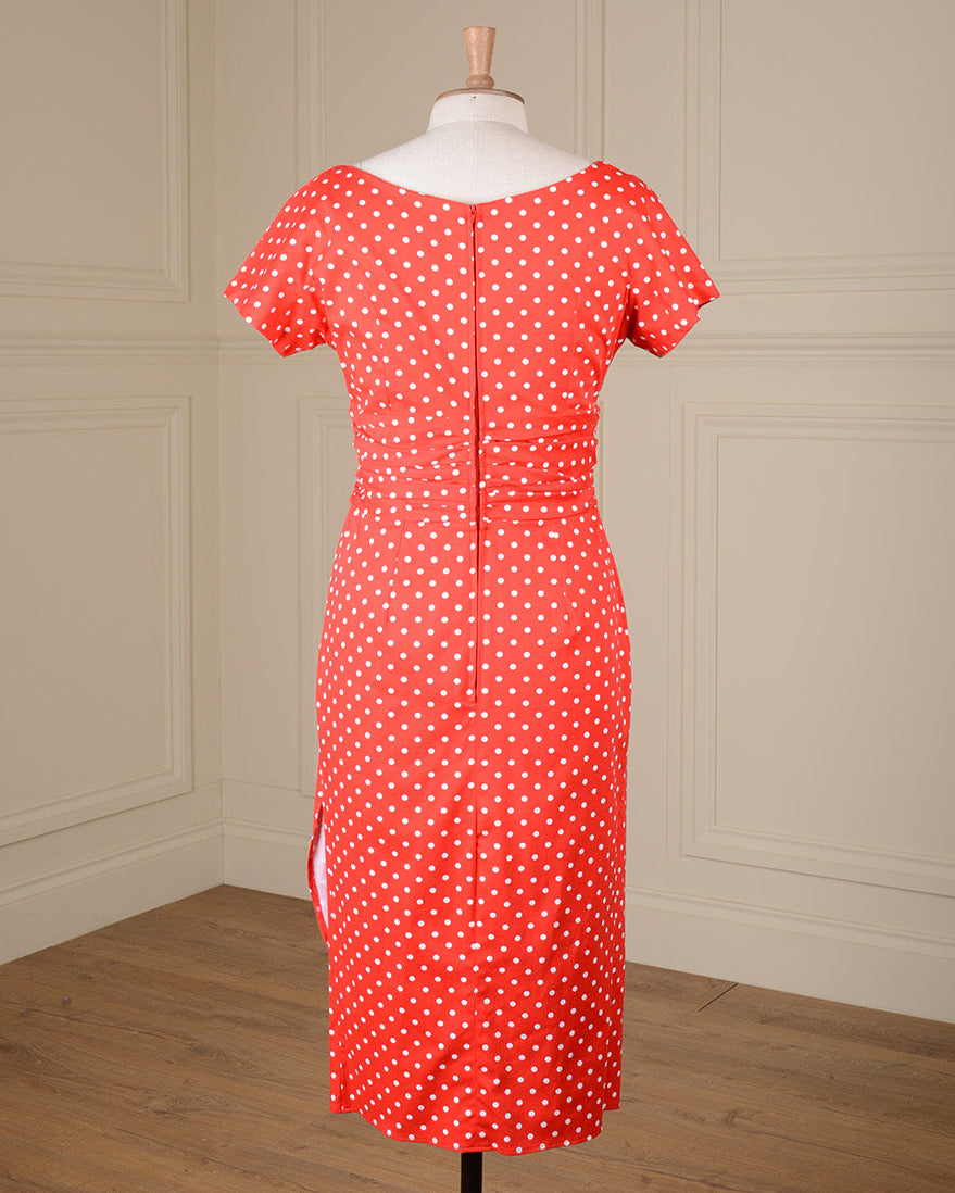 A red and white polka dot short-sleeve dress displayed on a mannequin in front of a cream paneled wall and wood floor.