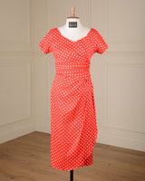 A red short-sleeve dress with white polka dots displayed on a white mannequin torso in a room with cream paneled walls and a wood floor.