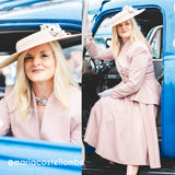 A woman wearing a dusty pink tailored suit, matching wide-brim hat with a flower accent, and white gloves sits in the open door of a vintage blue truck. The photo is a split composition with a close-up portrait on the left and a full-body seated pose on the right.