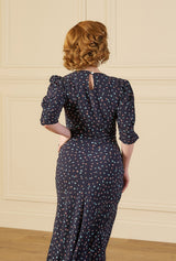 Woman wearing a 1940s print tea midi dress in ocean pearl navy dark blue dress with white patterns in a room with wooden floor and paneled walls.
