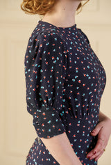 Woman wearing a 1940s print tea midi dress in ocean pearl navy dark blue dress with white patterns in a room with wooden floor and paneled walls.